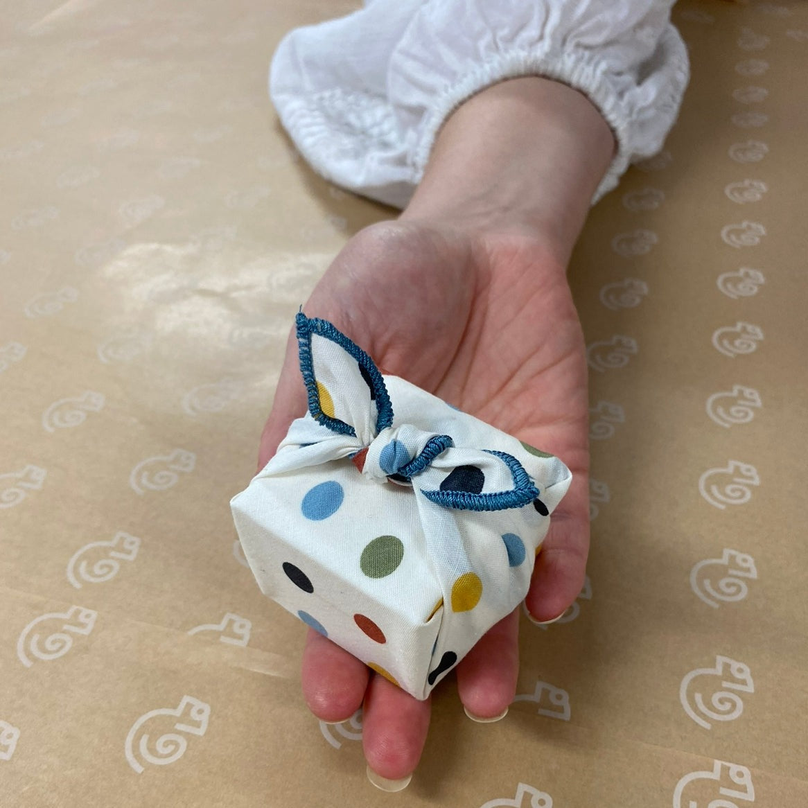 This Furoshiki or fabric gift wrap has cute spots and dots on a light cream background. The earthy multicoloured spots are red, yellow, green, blue, and black. They are solid colours and all the same size dots