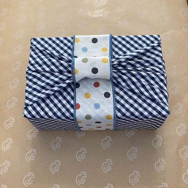 This is a picture of a medium black gingham (check) fabric gift wrap and the Furoshiki style knot is covered by our Earth spot belly band.. This fabric has cute spots and dots on a light cream background. The earthy multicoloured spots are red, yellow, green, blue, and black. They are solid colours and all the same size dots and look fabulous on the black gingham fabric gift wrap.