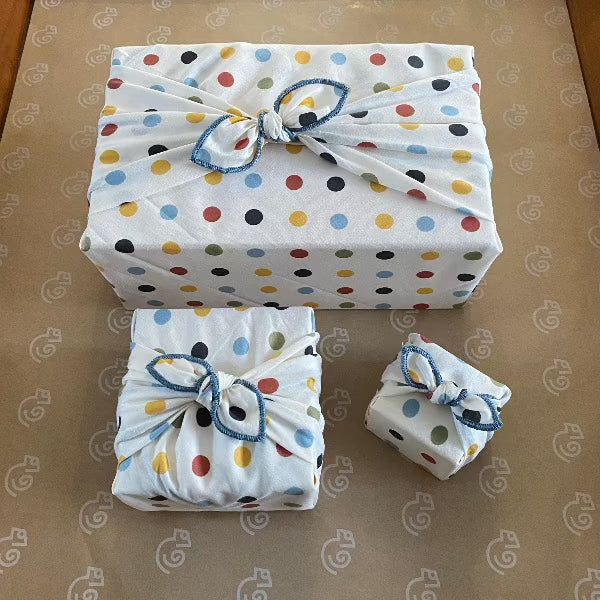 This Furoshiki or fabric gift wrap has cute spots and dots on a light cream background. The earthy multicoloured spots are red, yellow, green, blue, and black. They are solid colours and all the same size dots. This picture shows 3 different sizes, extra small, small, and medium.