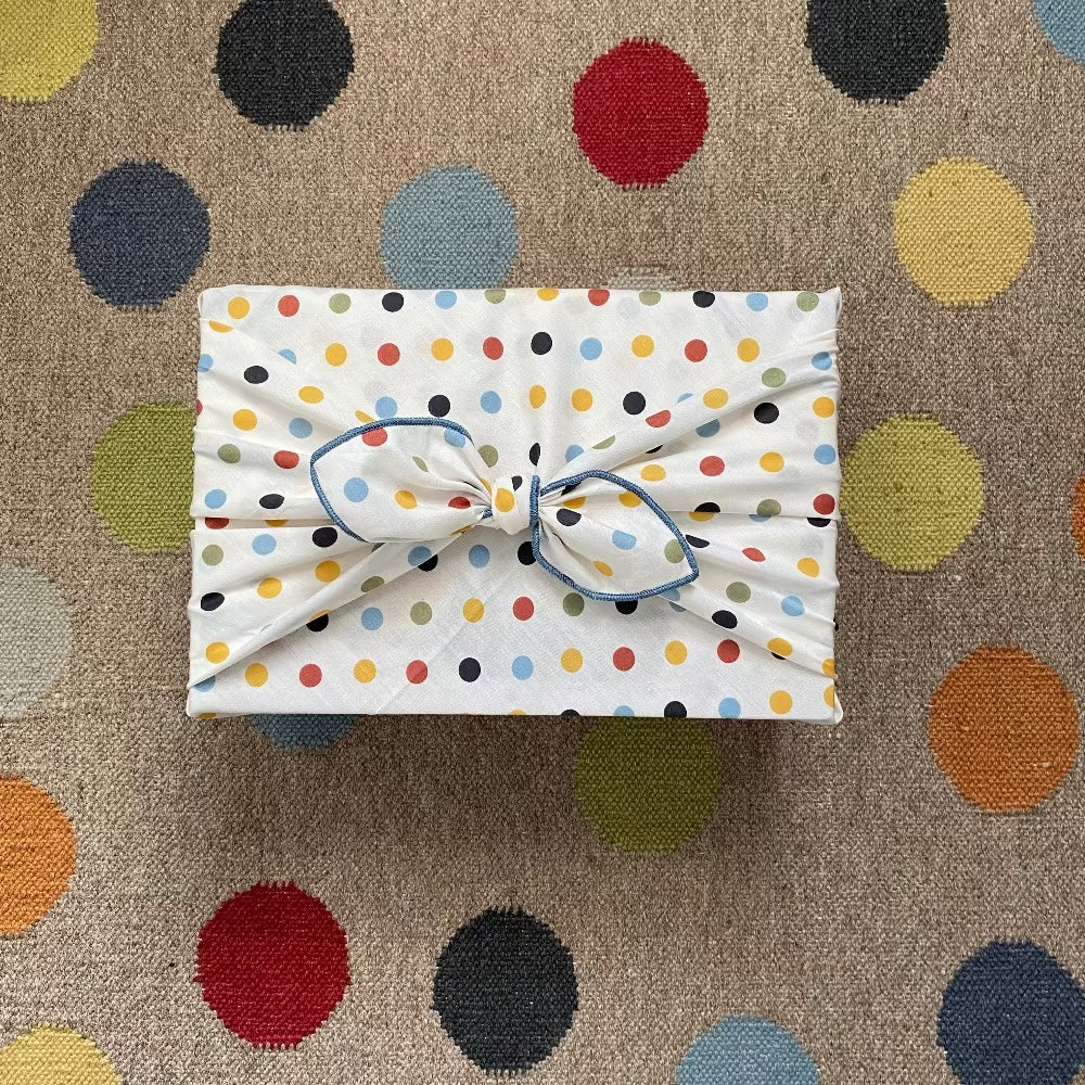 This Furoshiki or fabric gift wrap has cute spots and dots on a light cream background. The earthy multicoloured spots are red, yellow, green, blue, and black. They are solid colours and all the same size dots. This picture shows our large size wrap that is 70 x70cm and wraps larger size gifts. 